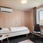 Schlafzimmer mit Bett, Stuhl und Fenster. Holzwände und Heizung sichtbar.