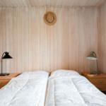 Zimmer mit zwei Betten, Holzwänden und Nachttischen mit Lampen.