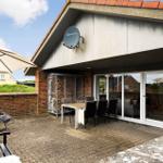 Terrasse mit Tisch, Stühlen, Sonnenschirm und Grill. Glasfront führt ins Haus.