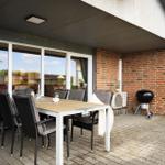 Terrasse mit Esstisch, Stühlen und Grill. Große Fensterfront. Ziegelmauer und Pflasterung.