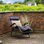 Liegende Sonnenliege auf Terrasse mit Steinmauer und Grünflächen im Hintergrund.