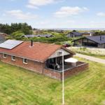 Ein Haus mit rotem Dach und Solarpanelen auf einer grünen Wiese mit Blick aufs Meer.