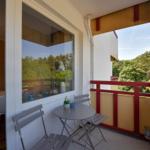 Balkon mit Tisch und Stühlen, rote Brüstung, Blick auf Bäume.