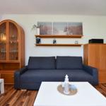 Wohnzimmer mit Sofa, Tisch und Holzmöbel. Wandbild und Küchenbereich sichtbar.