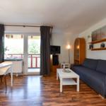 Wohn- und Essbereich mit Sofa, Tisch, TV und Balkon. Holzboden und Wandbilder.