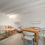 Wohn- und Essbereich mit Sofa, Tisch und Stühlen. Holzdecke und weiße Wände.