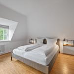 Schlafzimmer mit Doppelbett, Holzboden und Dachfenster mit Blick auf Bäume.