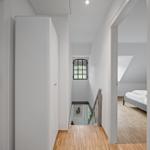 Flur mit Holzboden, Treppenhaus und Blick in Schlafzimmer mit Bett.
