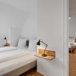 Zimmer mit Dachschrägen, zwei Betten und Holzfußboden. Fenster mit Blick auf Grün.