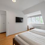 Doppelbettzimmer mit TV, Fenster und Holzboden. Tür führt in einen Flur.