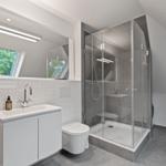 Badezimmer mit Dusche, Waschbecken und Toilette. Fenster mit Blick auf Grün.