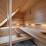 Holzsauna mit mehreren Sitzbänken, Thermometer und Eimer mit Löffel.
