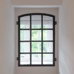Schwarzes Fenster mit Bogen oben, Blick auf grüne Bäume draußen.