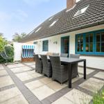 Terrasse mit Tisch, Stühlen und Strandkorb. Haus mit blauen Fenstern und Dachgauben.