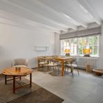 Wohn- und Essbereich mit Holztisch, Sitzmöbeln und Fenstern mit Blick auf Grün.