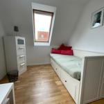 Schlafzimmer mit Dachschräge, weißem Bett und Holzboden. Fenster und Schrank sind sichtbar.