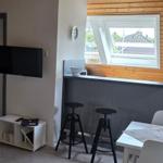 Wohnbereich mit TV, Esstisch und Barhocker. Holzwand und Dachfenster.
