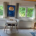 Esszimmer mit Tisch, Stühlen und Fenstern zum Garten. Wandmontierte TV und Deckenleuchte.