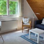 Wohn- und Essbereich mit Sofa, Tisch und Stühlen. Holzwand und Fenster mit Blick auf Grün.