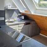 Küche mit Dunstabzug, Spüle und Fenster. Holzwand und dunkle Arbeitsplatte.