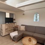 Wohnzimmer mit Ecksofa, runden Tisch und Fernseher an Wand.