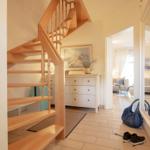 Hausflur mit Holztreppe, Schuhen und Kleidung. Im Hintergrund Wohnzimmer.