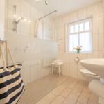 Badezimmer mit Dusche, Waschbecken und Fenster mit Blumen.