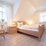 Schlafzimmer mit Holzbett, zwei Fenstern und TV-Schrank.