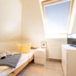 Schlafzimmer mit Dachschrägen, Bett, Nachttisch, Fernseher und Dachfenster.