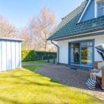Haus mit Terrasse, Garten und Liegestühlen. Blaue Fensterrahmen und grüner Dachfirst.