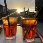Zwei Gläser mit Getränk stehen auf einem Tisch vor Sonnenuntergang.