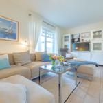 Wohnzimmer mit Sofa, Couchtisch und TV. Fenster mit weißen Vorhängen.