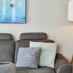 Graße Couch mit Kissen und Stehlampe neben Wandbild mit Segelbooten.
