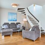 Wohnzimmer mit grauem Sofa, Treppenaufgang und Wandbild mit Segelbooten.