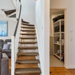 Treppenhaus mit Holzstufen führt zur oberen Etage. Wohnbereich mit Sofa und Wandbild.