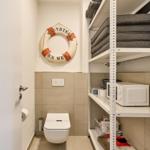 Toilette mit Rettungsring an der Wand und Metallregal mit Kissen und Mikrowelle.