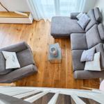 Ein Wohnzimmer mit grauem Sofa, Holzboden und Wandbild.