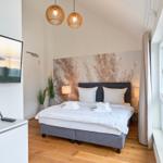 Schlafzimmer mit Bett, Fensterblick aufs Meer und Fernseher an der Wand.