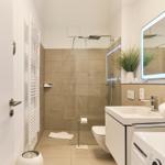 Badezimmer mit Dusche, Waschbecken und Toilette. Spiegel mit Beleuchtung und Pflanze.