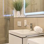 Bad mit Dusche, Waschbecken und beleuchtetem Spiegel.