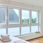 Ein Schlafzimmer mit großem Fenster, Blick auf Dach und Grün, Badetuch auf Bett, Wand-TV.