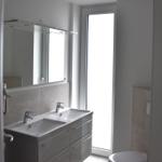 Badezimmer mit Waschbecken, Spiegel und Fenster.