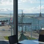 Tisch und Stühle vor großem Fenster mit Blick auf Hafen und Meer.