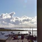 Aus dem Fenster blickt man auf einen Hafen mit Booten und einem Schiffssteg unter blauem Himmel mit Wolken.