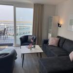 Wohnzimmer mit Sofa, Sessel und Tisch. Durchgang zur Terrasse mit Meerblick.