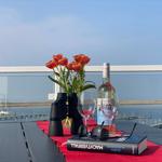 Tisch auf Balkon mit Tulpen, Wein, Fernglas und Buch vor Wasser.
