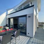 Terrasse mit Tisch, Stühlen und Blumen. Glasfront öffnet sich ins Innere.