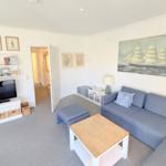 Wohnzimmer mit Sofa, Couchtisch und Fernseher. Wandbild zeigt Segelschiff.