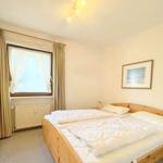 Schlafzimmer mit Holzbett, Kleiderschrank und Fenster mit Vorhängen.