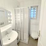 Badezimmer mit Dusche, Waschbecken und Toilette. Fenster mit Gitter.